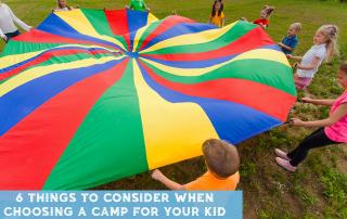 Kids at a day camp playing with a rainbow colored parachute outside.