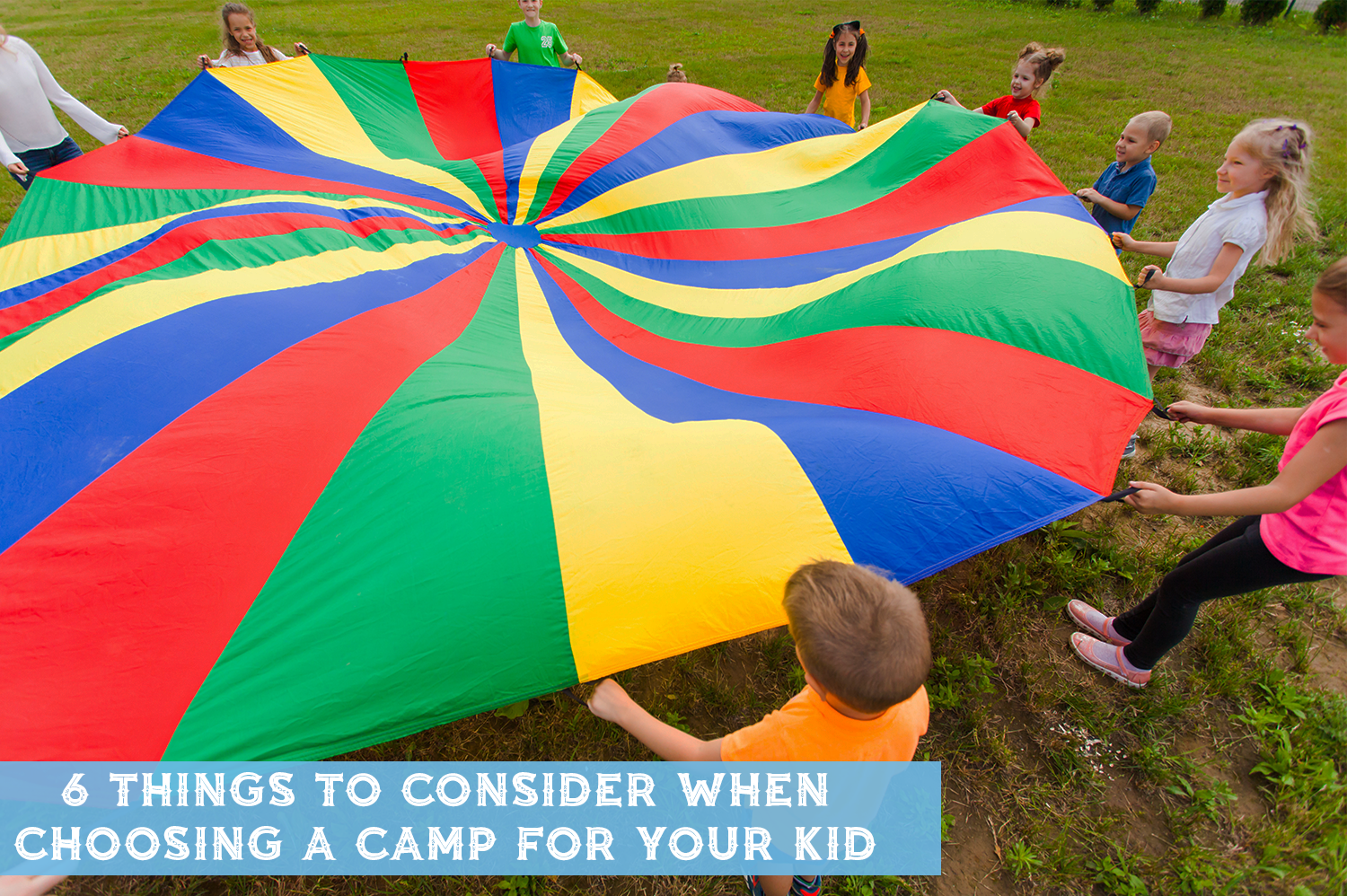 Kids at a day camp playing with a rainbow colored parachute outside.
